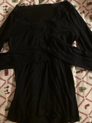 Svart långärmad blus med spets från intemissemi - Säljer en svart långärmad blus med v-ringning och fina spetsdetaljer längs halsringningen och vid ärmsluten. Blusen har en elegant och stilren look, perfekt att matcha med jeans eller kjol. Materialet känns mjukt och följsamt mot huden.