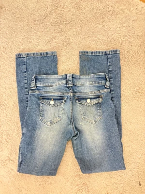 Blå bootcut jeans med slitningar - Snygga blå bootcut jeans med ljusa slitningar framtill och bak. Klassisk femficksmodell med dubbla knappar och dragkedja i midjan. Bakfickorna har lock och dekorativa knappar. Jeansen är tillverkade i jeansmaterial med en skön passform.