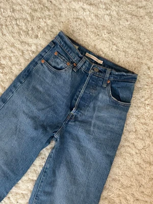 Levi's 501 blå jeans, straight fit - Säljer ett par klassiska Levi's 501 jeans i blå tvätt med raka ben och hög midja. Jeansen har fem fickor, knappgylf och snygga kopparfärgade nitar. Materialet är robust denim i bomull och passformen är straight. Perfekt för dig som gillar tidlös stil. Knappt använda 💞