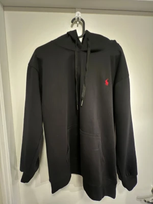 Polo hoddie  - Säljer en stilren svart hoodie från Polo Ralph Lauren med klassisk röd broderad logga på bröstet. Tidlös modell som passar till det mesta.  Detaljer: 	•	Färg: Svart 	•	Märke: Polo Ralph Lauren 	•	Modell: Hoodie med huva och magficka 	•	Skick: Mycket fint skick 	•	Passform: Bekväm och stilren  Perfekt för både vardag och fritid.