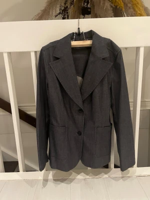 Mörkgrå kavaj från Filippa K XL - Snygg mörkgrå kavaj från Filippa K i storlek XL. Klassisk modell med två knappar framtill, breda slag och två framfickor. Materialet är bomull och polyester, vilket ger en stilren och bekväm känsla. Perfekt för dig som gillar en clean och enkel look.