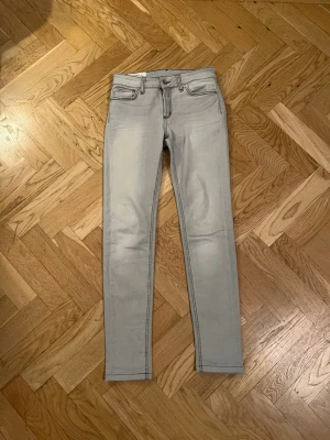 Ljusgrå slimfit jeans från Dondup - Säljer ett par ljusgrå slimfit jeans från Dondup, modell Tara. Jeansen har klassisk femficksdesign, svarta kontrastsömmar och läderpatch med logga bak. Tillverkade i bomull med stretch för skön passform. Perfekt för dig som gillar smal siluett och stilren look.