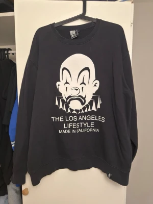 Svart sweatshirt från joker brand  - Cool svart sweatshirt med stor vit clown-tryck och texten 'The Los Angeles Lifestyle Made in California' på framsidan. Tröjan har rund hals och långa ärmar, perfekt för dig som gillar streetwear och oversized stil. Sitter som en 2xl