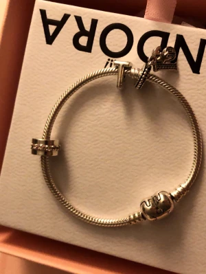 Pandora silverfärgad armband med berlocker - Snyggt armband från Pandora i silverfärgad metall med flera berlocker, bland annat ett hjärta med Pandora-logga, en ring med små stenar och en berlock med stjärna. Perfekt att mixa med andra smycken för en personlig stil.