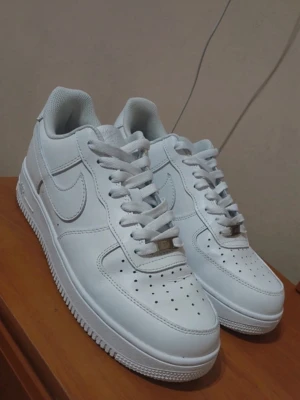 Nike Air Force 1 helvita sneakers - Klassiska Nike Air Force 1 sneakers i helvitt skinn med perforerad tå, rund tå och platt sula. Snygg och tidlös modell med snörning och diskret Nike-logga på sidan. Perfekta för dig som vill ha en clean och stilren look. Skriv till mig för funderings ekan gå ner i pris vid snabb affär