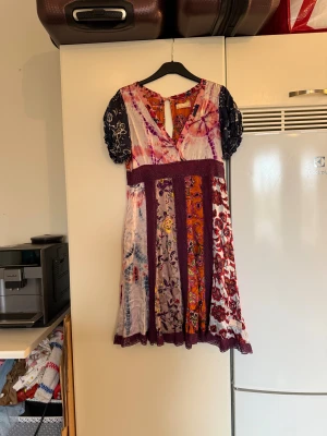 Odd Molly blommig kortklänning, strl 2 - Färgstark och unik kortklänning från Odd Molly med blommigt mönster i lila, orange, marinblå, rosa och vitt. Klänningen har v-ringning, kort puffärm och dekorativa spetsdetaljer i midjan och nederkant. Materialet är mjukt  och flowy, perfekt för dig som gillar boho vibes. Från märket Odd Molly. Storlek 2 som enligt deras storleksguide motsvarar en M. Fin men se sista bild för lite anmärkning. 