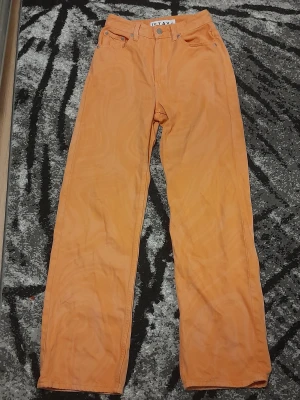 Orange raka jeans från STAY - Säljer ett par orange jeans från STAY med klassisk femficksdesign och raka ben. Byxorna har hög midja och är tillverkade i ett mjukt bomullsmaterial. Perfekt för dig som vill sticka ut med färg och gillar en avslappnad passform.