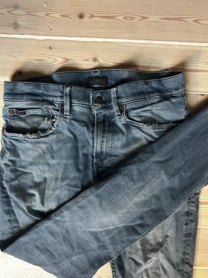 Blå jeans från Polo Ralph Lauren - Snygga blå jeans från Polo Ralph Lauren i klassisk femficksmodell. Jeansen har slitna detaljer vid fickorna och är tillverkade i ett mjukt bomullsmaterial med lite stretch. Passformen är rak och midjan är normal. Perfekt för dig som gillar en avslappnad stil. Skick: 8/10. Nypris: 2999kr