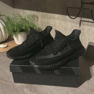 Adidas Yeezy Boost 350 V2 Black - Säljer ett par Adidas Yeezy Boost 350 V2 i helsvart färg. Skorna har stickad ovandel i syntet, klassisk Yeezy-silhuett och svart sula med ribbad struktur. Sidan pryds av den ikoniska SPLY-350-texten. Perfekta för dig som gillar streetwear och vill ha något unikt.
