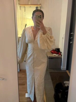 Adoore klänning  - Säljer en långklänning i ljusbeige med tunna bruna ränder. Klänningen har djup v-ringning, puffiga långärmar och knappar framtill hela vägen ner. Materialet känns som bomull och den har en slits framtill för extra rörelsefrihet. Klänningen är från Adoore och prislappen sitter kvar. Endast testad. Säljs inte längre på Adoore hemsidan 