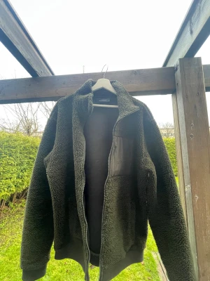 Grön teddyjacka Peak Performance XL - Mysig grön teddyjacka från Peak Performance i storlek XL. Jackan har en bröstficka med dragkedja och broderad logga, samt hel dragkedja framtill. Materialet är fluffigt fleece och jackan har långärmade ärmar och ribbade muddar. Går att anända som L!