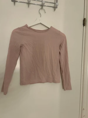 Ljusrosa långärmad topp från H&M - Säljer en enkel och mjuk ljusrosa långärmad topp från H&M Basic, tillverkad i ekologisk bomull. Modellen är rak med rund halsringning och har en clean look utan mönster eller detaljer. Perfekt att matcha med jeans eller kjol.