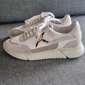 Axel Arigato Genesis  - Snygga sneakers från Axel Arigato med broderad fågel på sidan. Modellen Genesis Neo Bird Runner är vit och beige. Riktigt fet combo🔥använd ett par gånger enbart men i riktigt bra skick. (Köpt för 2800) (säljs för 1500kr)
