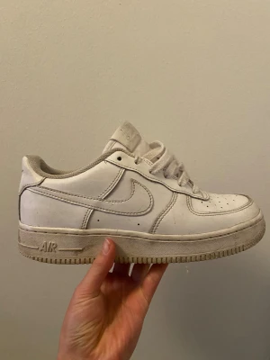 Nike Air Force 1 vita sneakers - Nike Air Force 1 sneakers i helvitt med klassisk låg siluett och rund tå. Skorna har snörning, perforerad tåbox och platt sula med Air-dämpning 