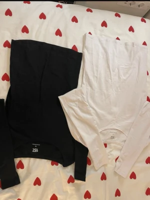 Svart och vit långärmad topp från 152 - Två stilrena långärmade toppar i svart och vitt från 152. Båda har rund hals och är tillverkade i mjuk bomull, perfekta att matcha med jeans eller kjol. Enkel design utan mönster eller detaljer, passar dig som gillar basic och cleant.
