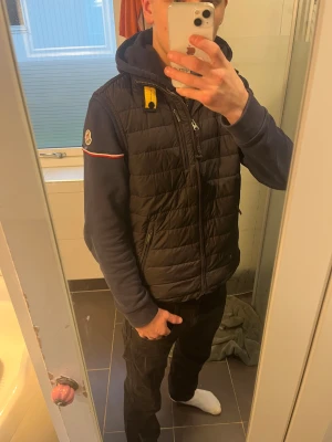 Svart dunväst från Parajumpers - Säljer en svart/mörkt grå, dunväst ifrån parajumper, den är i storlek y-l och passar bra ifrån 168-174, den har 3 små hål, 1 lagat lite halvt, detta är absolut inget man tänker på, ger ett väldigt bra helhetsintryck och man ser i princip nästan inte hålen