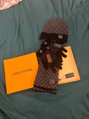  halsduk set i svart/grå - Snyggt halsdukset med mössa och vantar med matchande mössa och handskar.mössan har litet hål. Setet är svart och grått med klassiskt rutigt LV-mönster och broderad logga på alla delar. Perfekt accessoar för kalla dagar och ger en lyxig touch till din outfit. PERFEKT JULKLAPP TILL EN NÄRA. Lägg prisförslag!