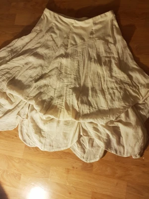 Elegant krämvit ballongkjol-Romantisk & Tidlös (strl 40 - Fluffig och romantisk vit långkjol från KappAhl med vågig nederkant och bred linning. Kjolen har ett skirt, lager-på-lager-utseende och är tillverkad i ett lätt tyg som ger en drömmig känsla. Perfekt för dig som vill ha en bohemisk och luftig stil.