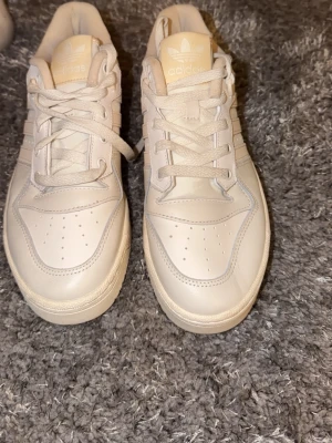 Adidas vita sneakers stl 40 - Fräscha vita Adidas sneakers med klassiska tre ränder på sidan och snörning framtill. Skorna har en rund tå och platt sula, tillverkade i skinn med diskreta detaljer. Perfekta för dig som gillar stilrena och cleana sneakers.