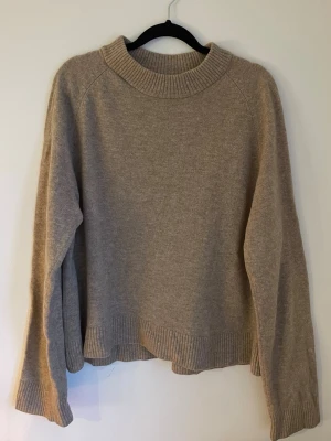 Beige stickad tröja från Wera - Säljer en beige stickad tröja från Wera i storlek M. Tröjan har en bred ribbad krage, långa ärmar och ribbade muddar vid ärmslut och nederkant. Perfekt för kyliga dagar och enkel att matcha med jeans eller kjol.