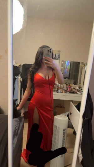 Röd långklänning med slits - Säljer en snygg röd långklänning med smala axelband och djup v-ringning. Klänningen har en hög slits på sidan som ger en extra touch. Materialet är glansigt och känns lyxigt, perfekt för att sticka ut. Passformen är tight och framhäver figuren.