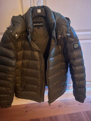 Mörkgrön pufferjacka från Bvaldi - Snygg mörkgrön pufferjacka från Bvaldi med huva och dragkedja framtill. Jackan har quiltad design, två sidofickor med dragkedja och en patch med logga på ärmen. Perfekt för kalla dagar och har en modern, loose passform. Påse med kommer. Köpte förra vinter och använts 2-3 gånger pris inte hugget i sten skriv vid funderingar🤗🤗