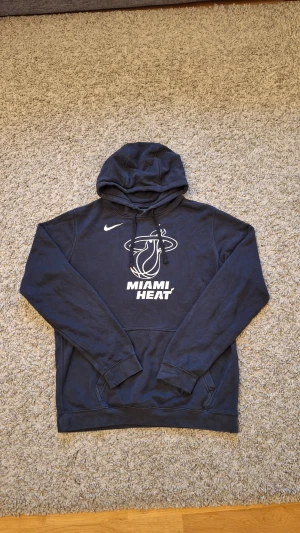 Svart Nike Miami Heat hoodie - Snygg skön svart Miami Heat hoodie från Nike i storlek M. Skicket är okej med lite slitningar då den har använts mycket(fråga gärna för fler bilder). Men det påverkar inte hoodiens skick som helhet. Passar riktigt bra för dig som gillar basket och håller på Miami Heat. Skick: 7/10