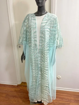 Ljusblå långklänning i mesh - Superfin långklänning i ljusblå mesh med vågiga broderade detaljer. Klänningen är transparent och har lös passform med korta ärmar. Perfekt för dig som vill sticka ut med en unik och luftig look.