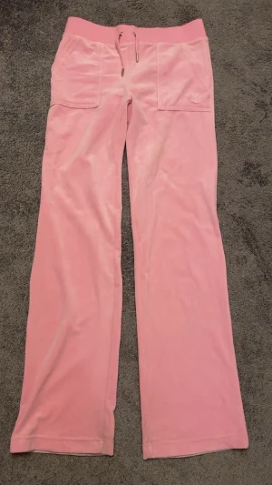 Rosa mjukisbyxor med snörning - Säljer ett par ljusrosa mjukisbyxor med bred resår och snörning i midjan. Byxorna har stora fickor fram och bak, samt silverfärgade detaljer på bakfickorna. Materialet är mjukt och har en lätt glansig finish som ger en chill vibe.