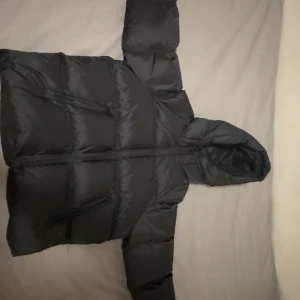 Svart pufferjacka från Zara med huva - Svart pufferjacka från Zara i storlek S. Jackan har en stor, mysig huva och två sidofickor med dragkedja. Den är quiltad och har en clean look med raka linjer. Perfekt för kalla dagar när du vill hålla dig varm och samtidigt se chill ut. Ny pris = 850