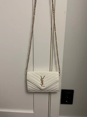 Vit ysl väska  - ✨ Vit YSL-väska – vitt & guld ✨ Vit YSL-väska i elegant vitt med gulddetaljer. Väskan är i mycket fint skick. Endast två små rosa fläckar som enkelt kan tas bort med sminkborttagning.  📦 Skickas samma dag som ordern läggs.