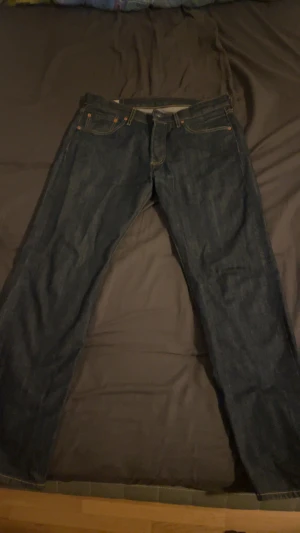 Levi's 501 jeans mörkblå - Klassiska Levi's 501 jeans i mörkblå denim med raka ben och knäppning i midjan. Snygga kontrastsömmar och ikonisk läderpatch bak. Perfekta för dig som gillar tidlös stil och vill ha ett par jeans som funkar till allt. Storlek W31/L30. Säljer dem pga att dem är för korta för mig. Men dom är ungefär som nya förutom den lilla defekten vid knäppningen. Pris kan diskuteras vid snabbaffär, hör gärna av er😁