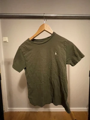 Olivgrön t-shirt från Ralph Lauren - Olivgrön t-shirt från Ralph Lauren med klassisk broderad logga på bröstet. T-shirten har rund halsringning och korta ärmar. Tillverkad i mjuk bomull för en skön känsla och avslappnad passform.