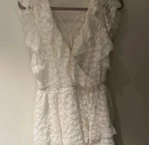 Vit spetsklänning med volanger från Nelly - Supersöt vit kortklänning från Nelly i spets med volanger och omlottkänsla. Klänningen har knyt i ryggen och är ärmlös med romantiska detaljer. Perfekt för sommaren och nu till studenten och midsommar! Pris kan diskuteras 🩷🤗🥂 