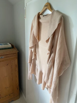 Ljusrosa kofta med volang från Gina Tricot - Supersnygg ljusrosa kofta från Gina Tricot i storlek L. Koftan har långa ärmar, bred krage och coola volangdetaljer längs fram och nederkant. Mjuk stickad kvalitet som är perfekt för lager-på-lager och chill vibes.