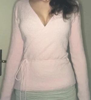 Ljusrosa omlottkofta med snörning - Säljer en superfin ljusrosa omlottkofta med snörning i midjan. Koftan har v-ringad hals och långa ärmar, perfekt för dig som gillar mjuka och mysiga plagg. Materialet känns fluffigt och passar extra bra när det är lite kyligt ute.