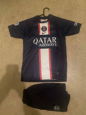 PSG Messi #30 matchtröja Nike - Säljer en blå Paris Saint-Germain fotbollströja med Messi #30 på ryggen och Qatar Airways-tryck på bröstet. Tröjan har korta ärmar, röd och vit rand i mitten och PSG-logga. Materialet är lätt och andas, perfekt för fotbollsträning eller match.