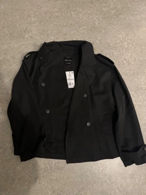 Helt ny svart trenchcoat från Stradivarius, stl S - Stilren svart rock från Stradivarius i storlek S. Jackan har dubbelknäppning, klassisk krage och axelklaffar. Perfekt för dig som gillar en clean och tidlös look. Materialet är mjukt och lätt, vilket gör den enkel att bära över olika outfits.