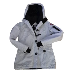 Vit dunjacka från Canada Goose - Säljer en vit dunjacka från Canada Goose med svart innerfoder och huva. Jackan har stora knappar, dragkedja, fickor med lock och en patch på ärmen. Materialet är polyester och bomull med fyllning av ankdun. Perfekt för kalla dagar och riktigt snygg streetstil.