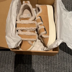 Inukii - Beigea sneakers - Säljer ett par beigea sneakers från Inukii med fluffiga teddy-detaljer och breda kardborreband. Skorna har en platt vit sula och är fodrade med mjukt teddy-material för extra komfort. Perfekt för dig som gillar mysiga och unika sneakers med cool design.                                                                         Säljer dessa på grund av för stor storlek för mig, och därför endast använda en gång! Annars normal i storlek men jag chansade för min storlek var slutsåld.