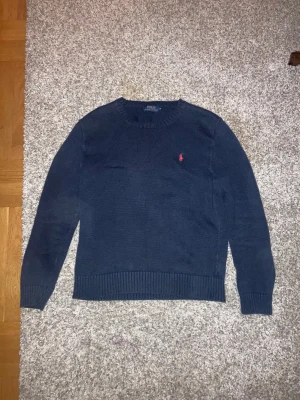 Ralph Lauren tröja - Snygg marinblå stickad tröja från Polo Ralph Lauren i storlek M. Tröjan har rund hals, ribbade muddar och ett rött broderat Polo-logo på bröstet. Passar dig runt 180 cm Nypris:1500kr Mitt pris:600kr