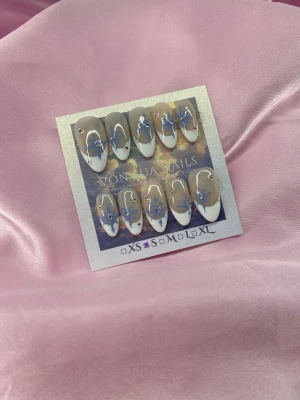 Snowflake ❄️(S);Medium Almond - Handgjorda press on-naglar i en medium mandelform med nude bas, vit fransk tipp och blå snöflingor dekorerade med små silverstenar. Snygg och trendig design som verkligen sticker ut. Perfekt för dig som vill ha unika naglar utan att gå till salong.