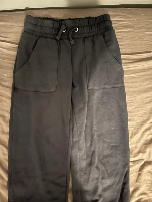 Svarta mjukisbyxor med snörning XS lager 157 - Svarta mjukisbyxor i storlek XS med bred resår och snörning i midjan. Byxorna har stora fickor framtill och är tillverkade i mjukt bomullsmaterial. Perfekta för chill dagar eller när du vill vara bekväm men ändå se stilren ut. Kostade (200)kr från början 