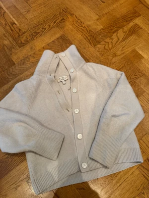 Ljusgrå kofta från & Other Stories - Supermysig ljusgrå kofta från & Other Stories med hög krage och stora vita knappar framtill. Koftan är stickad i mjuk kashmir och har långa ärmar med breda ribbade muddar. Perfekt för lager-på-lager och chill dagar.