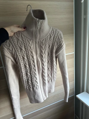 Beige kofta - Beige stickad kofta med hög krage och dragkedja. Använd sparsamt! 