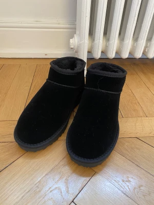 Svarta mockaboots med pälsfoder - Mysiga svarta boots  med mjukt pälsfoder på insidan. De har en rund tå och platt sula med mönstrad undersida för extra grepp. Perfekta för kalla dagar och har en enkel, stilren design som passar till det mesta.