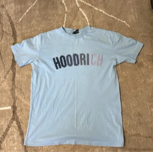 Ljusblå HOODRICH t-shirt - Snygg ljusblå t-shirt från HOODRICH med tryckt logga i svart och vitt över bröstet. Klassisk passform och rund halsringning, perfekt för en chill streetwear-look.