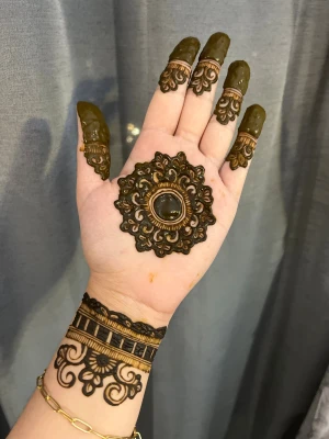 Brunt henna-armband med blommönster - Unikt henna-armband med detaljerat blommönster i brunt och svart, som sträcker sig över handleden och fingrarna. Designen har en stor blomformad cirkel på handflatan och eleganta mönster på fingertopparna. Perfekt för dig som vill sticka ut med konstnärliga detaljer.
