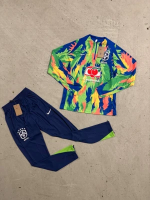 Nike Brasil långärmad träningströja - Säljer en Nike Brasil långärmad träningströja med färgstarkt mönster i blått, grönt, gult och orange. Tröjan har half zip och Brasil-logga på bröstet. Perfekt för fotbollsträning och har en sportig vibe med coola färgdetaljer. Passar S/M