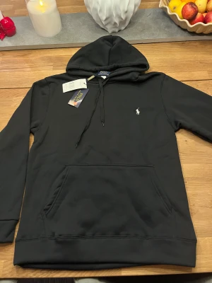 Svart hoodie från Polo Ralph Lauren - Svart hoodie från Polo Ralph Lauren i storlek S. Klassisk design med huva och snörning, stor magficka och den ikoniska broderade loggan på bröstet. Mjuk och skön bomullsmix som passar perfekt när du vill ha en chill och stilren look. Pris kan diskuteras.